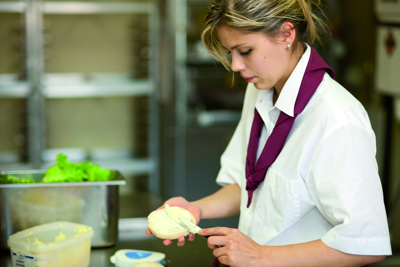 Verkäuferin schmiert Butter auf Brötchen