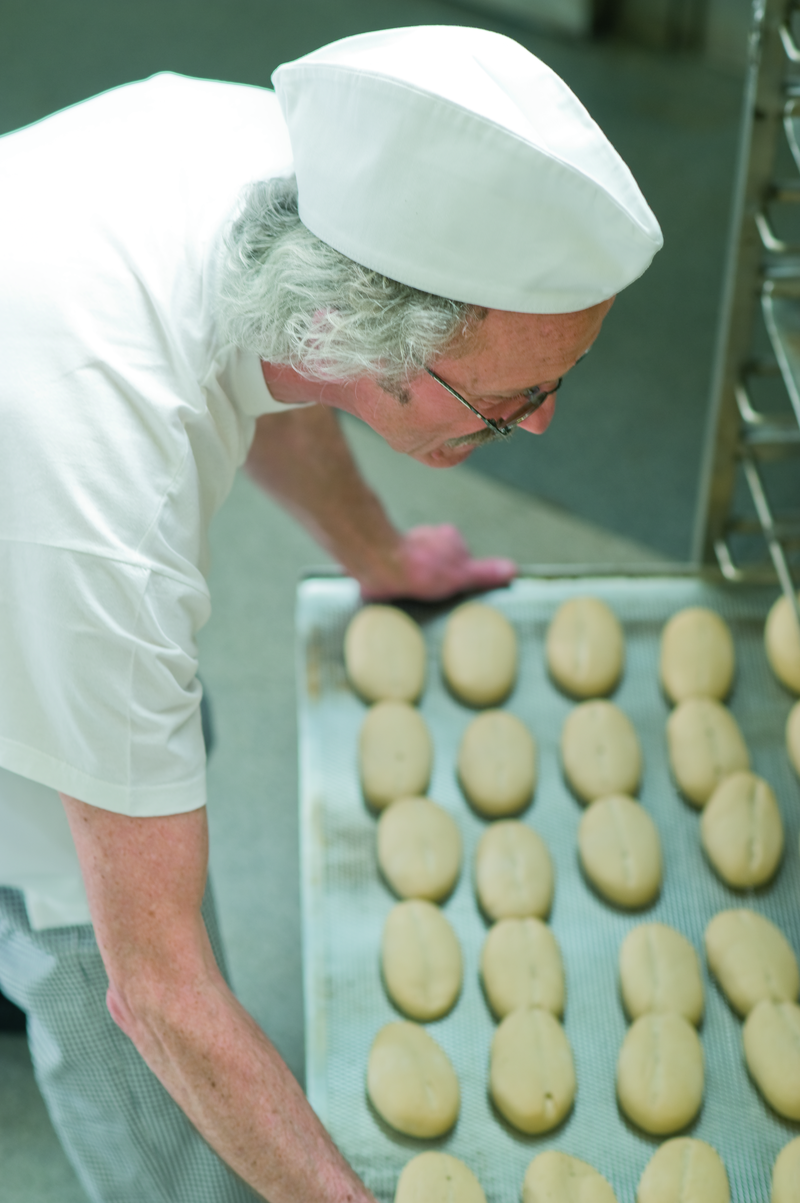 Bäckermeister schiebt ein Backblech mit Brötchenteiglingen in einen Stikken