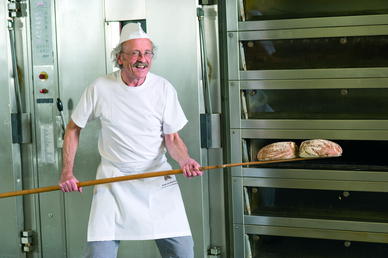 Bäckermeister backt mit einem Schießer Brote aus einem Etagenofen aus
