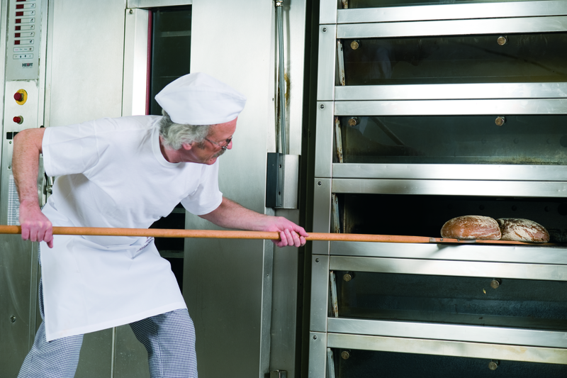 Bäckermeister backt mit einem Schießer Brote aus einem Etagenofen aus