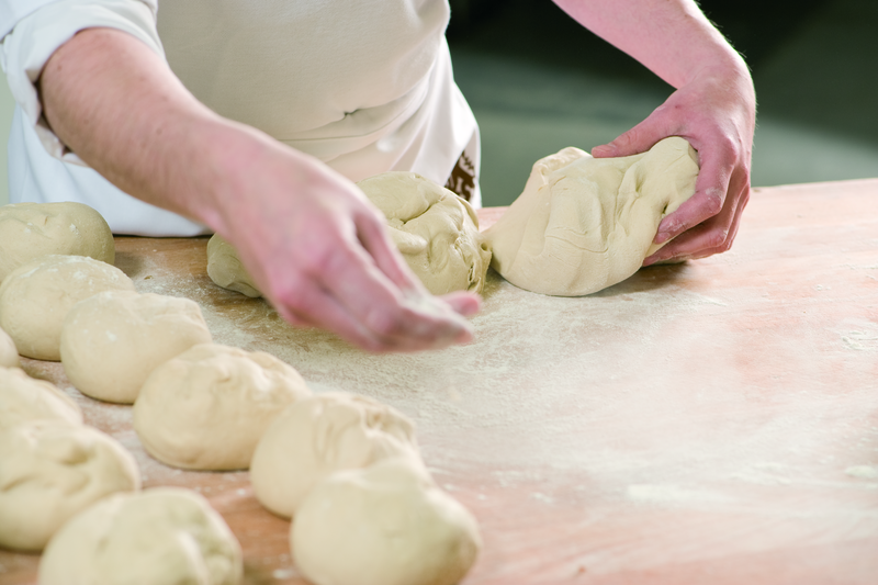 Bäcker vearbeitet Teig zu Brötchenteiglinge an einer Tafel