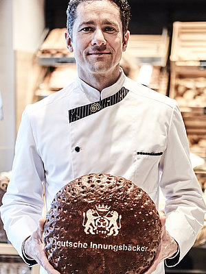 Bäckereifachverkäufer hält Brot in die Kamera 