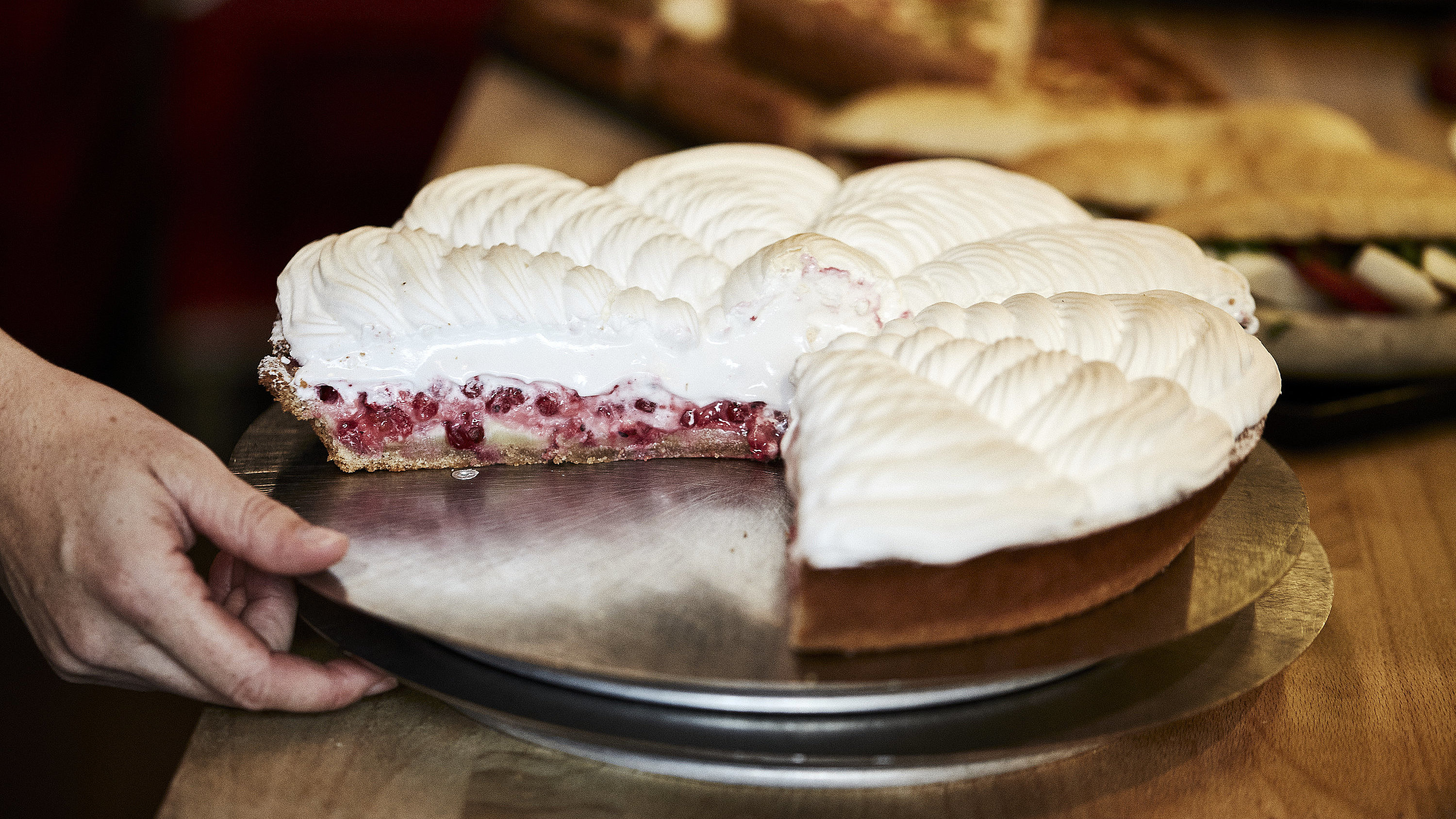 Angeschnittene Himbeer Baiser Torte auf einem Tablett, nach dem eine Hand greift