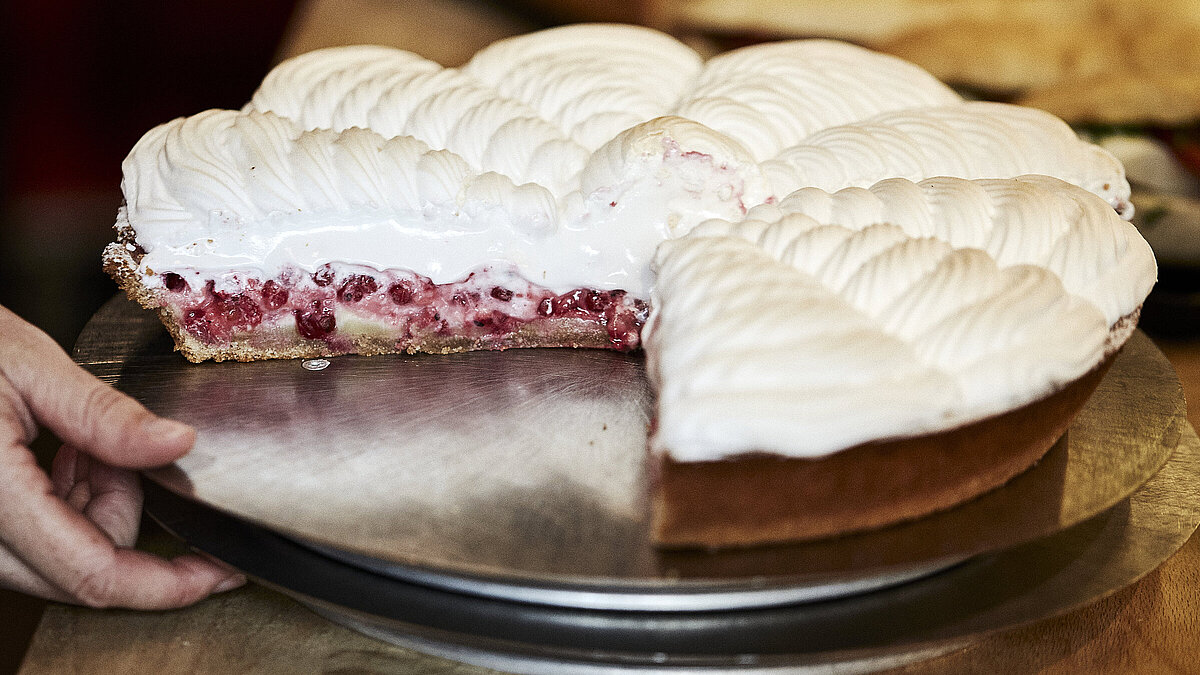 Angeschnittene Himbeer Baiser Torte auf einem Tablett, nach dem eine Hand greift