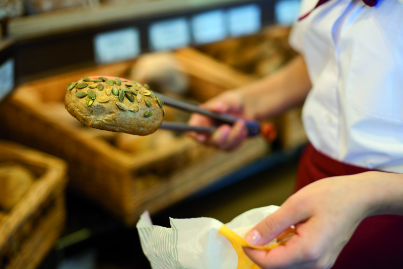 Verkäuferin packt Kürbiskernbrötchen in Tüte