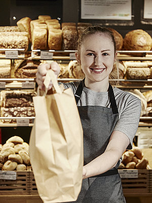 Bäckereifachverkäuferin reicht eine volle Bäckertüte