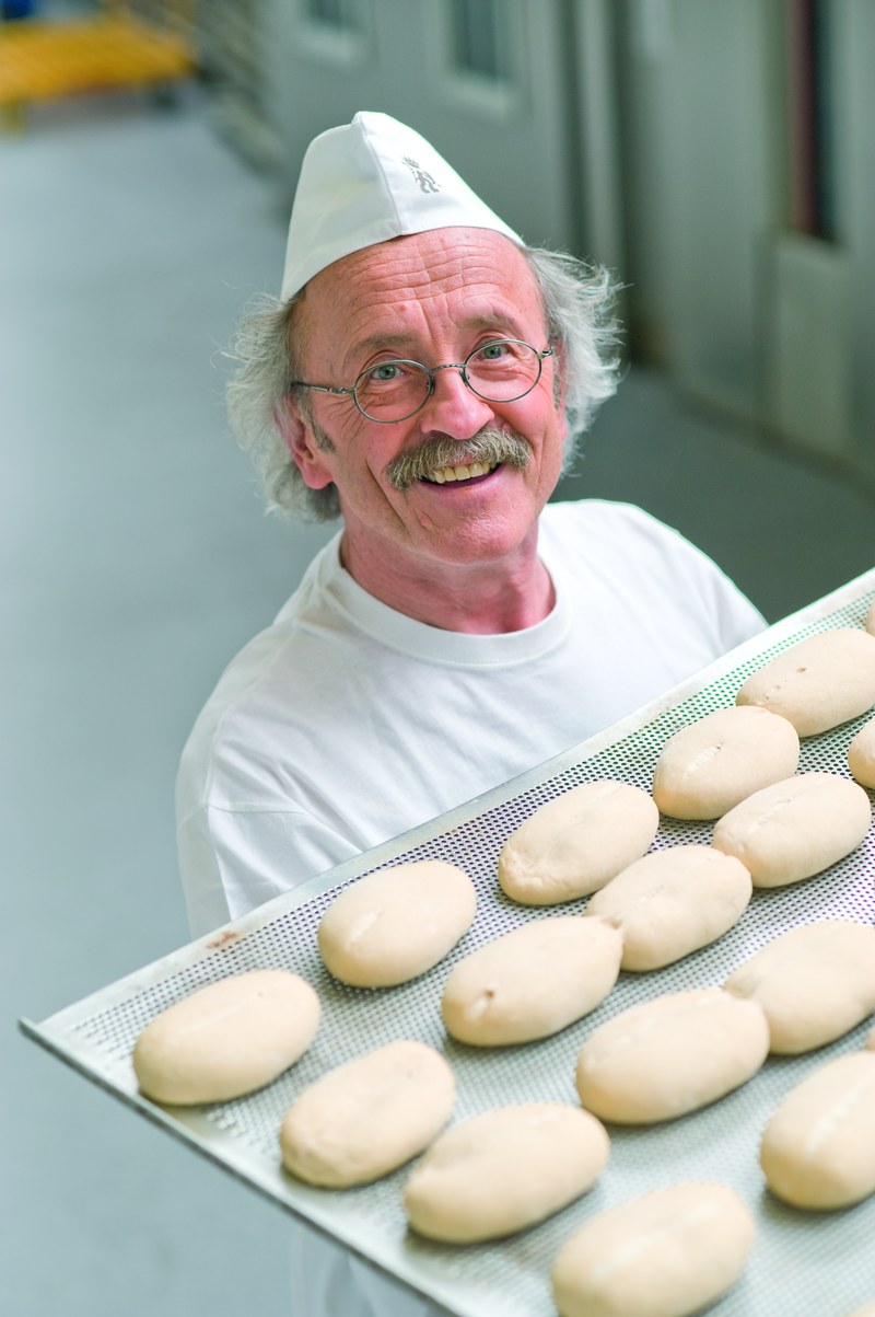 Bäckermeister trägt ein Backblech mit Brötchenteiglingen