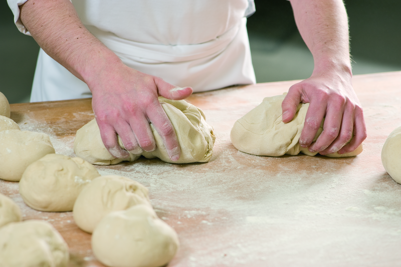 Bäcker vearbeitet Teig zu Brötchenteiglinge an einer Tafel