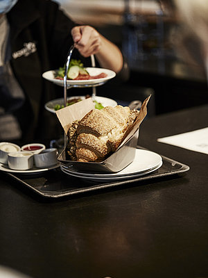 Croissant wird auf einem Teller serviert. Im Hintergrund ist eine Etagiere mit Aufschnitt zu sehen.