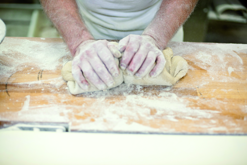 Bäcker knetet Teig auf bemehlter Oberfläche