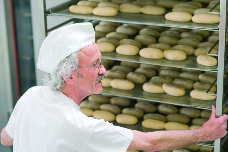 Bäckermeister schiebt einen Stikken mit Brötcheteiglingen