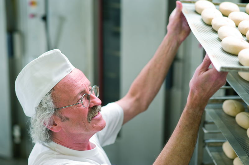 Bäckermeister schiebt ein Backblech mit Brötchenteiglingen in einen Stikken