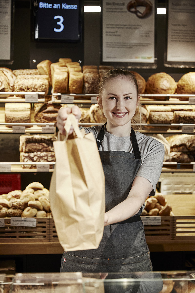 Verläuferin reicht Tüte über Tresen