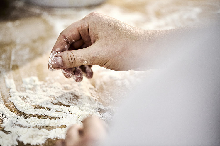 Detailaufnahme einer Bäckerhand, die Mehl auf einer Arbeitsfläche verteilt.