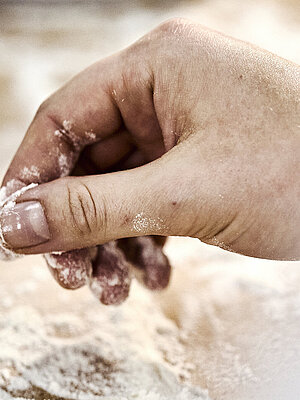 Detailaufnahme einer Bäckerhand, die Mehl auf einer Arbeitsfläche verteilt.