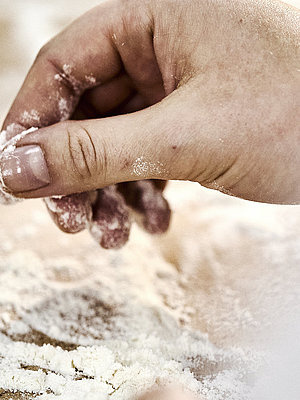 Detailaufnahme einer Bäckerhand, die Mehl auf einer Arbeitsfläche verteilt.