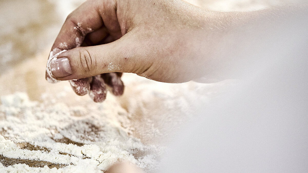 Detailaufnahme einer Bäckerhand, die Mehl auf einer Arbeitsfläche verteilt.