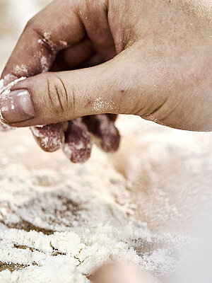 Detailaufnahme einer Bäckerhand, die Mehl auf einer Arbeitsfläche verteilt.