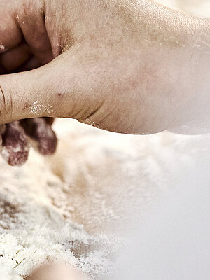 Detailaufnahme einer Bäckerhand, die Mehl auf einer Arbeitsfläche verteilt.