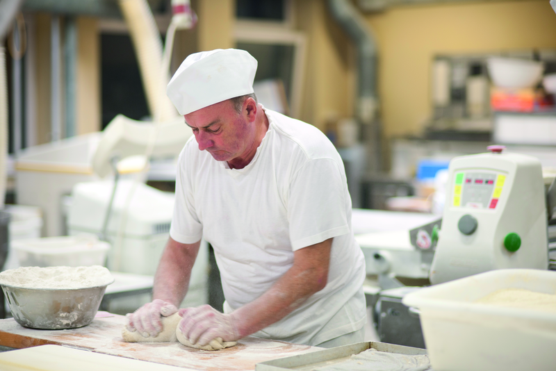 Bäcker knetet Teig auf bemehlter Oberfläche