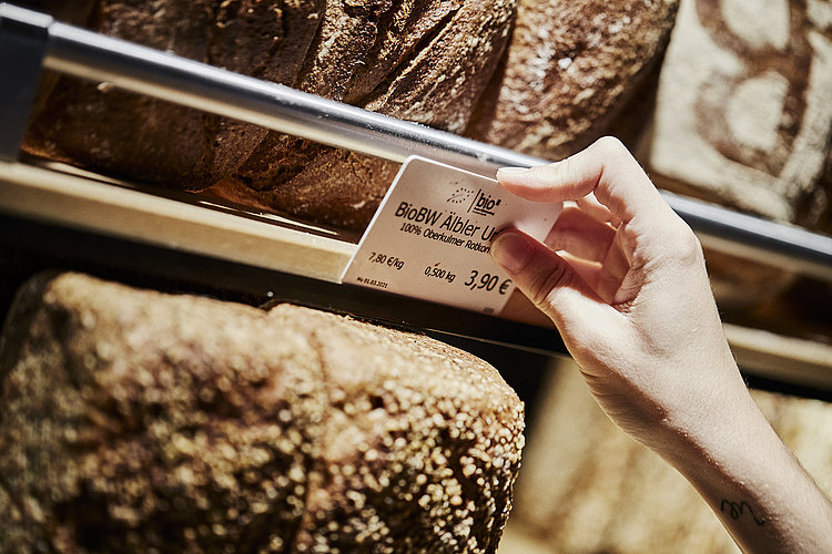 Preisschild für ein Brot wird an der entsprechenden Halterung angebracht. zu Sehen sind diverse Brote