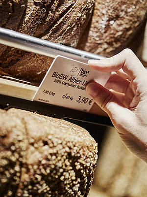 Preisschild für ein Brot wird an der entsprechenden Halterung angebracht. zu Sehen sind diverse Brote