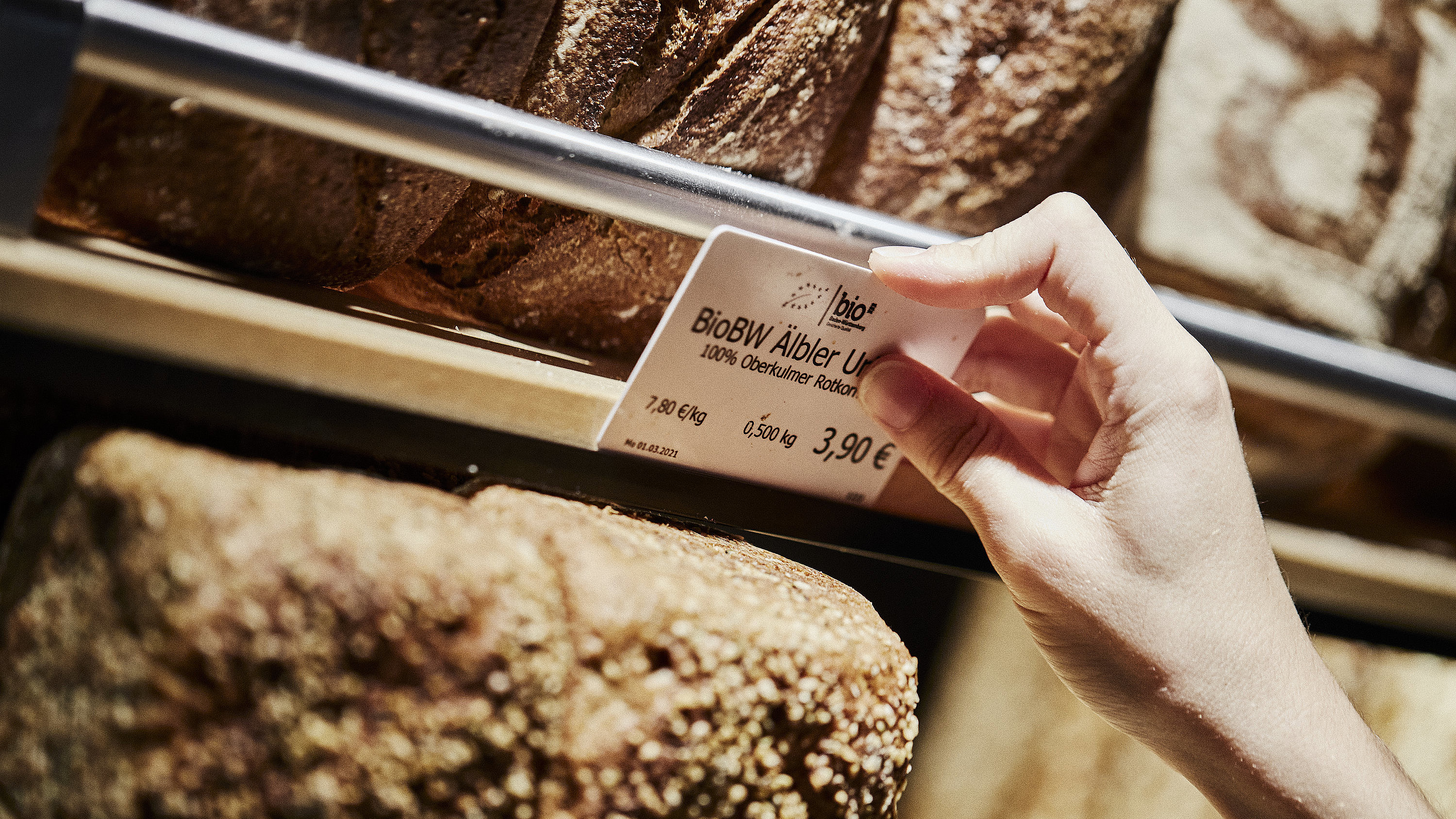 Preisschild für ein Brot wird an der entsprechenden Halterung angebracht. zu Sehen sind diverse Brote