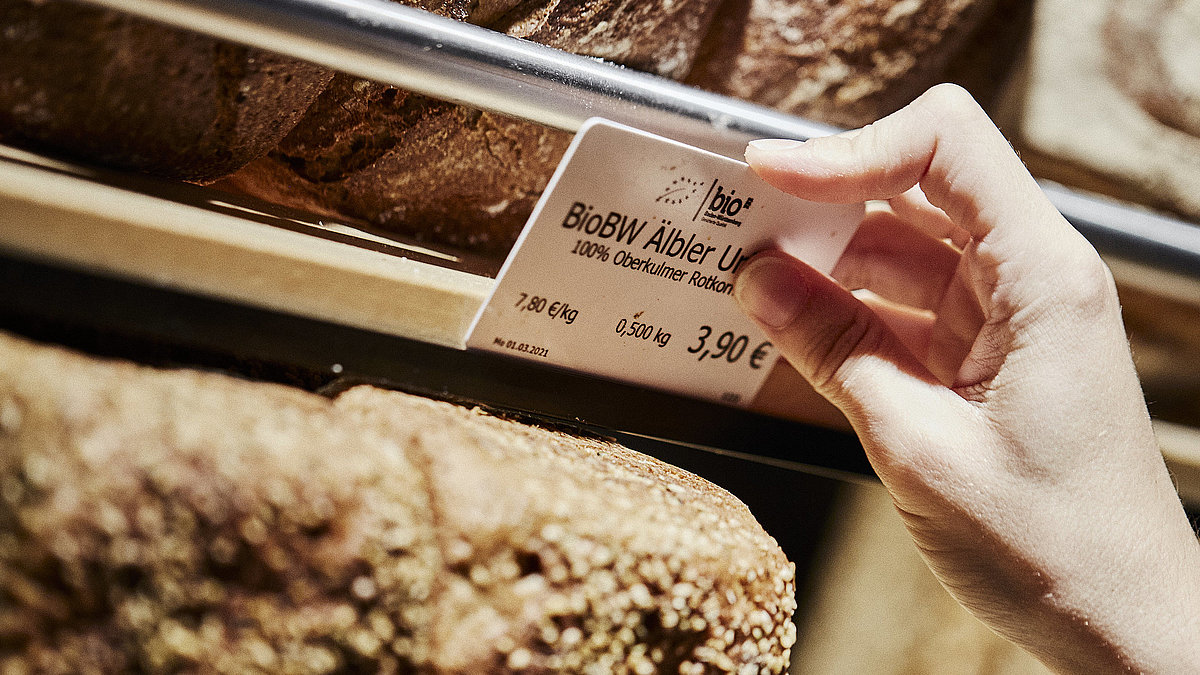 Preisschild für ein Brot wird an der entsprechenden Halterung angebracht. zu Sehen sind diverse Brote