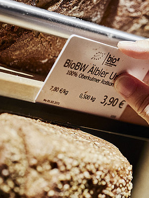 Preisschild für ein Brot wird an der entsprechenden Halterung angebracht. zu Sehen sind diverse Brote