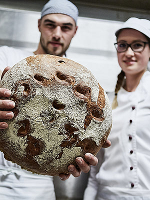 Bäcker hält ein Laib Brot in die Kamera